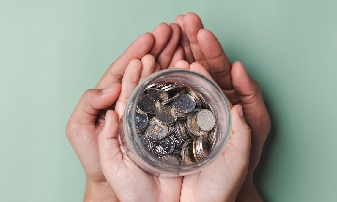 Two overlapped hands hold a jar of money