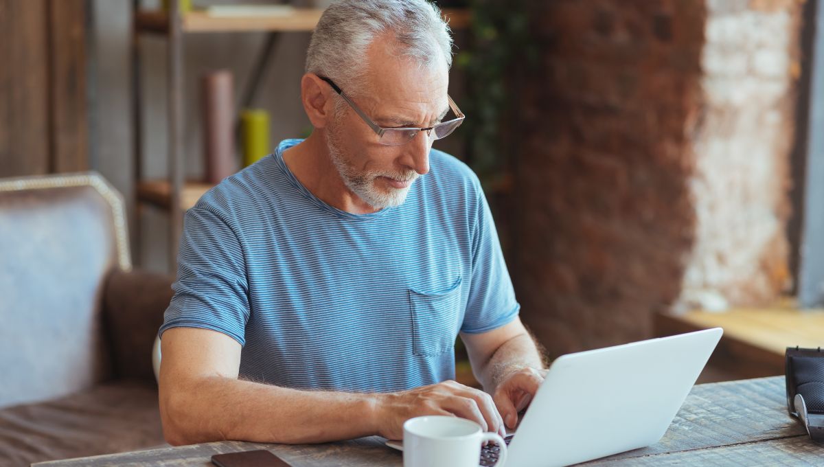 Elderly man using his computer while taking a cup of tea