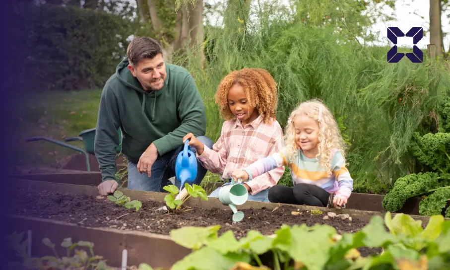 A man and two children outside smiling while they water plants