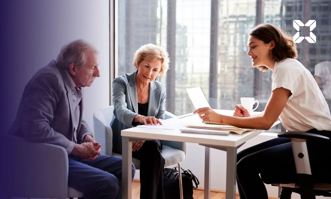 Financial adviser sitting at a desk with a retired couple, reviewing paperwork in an office.