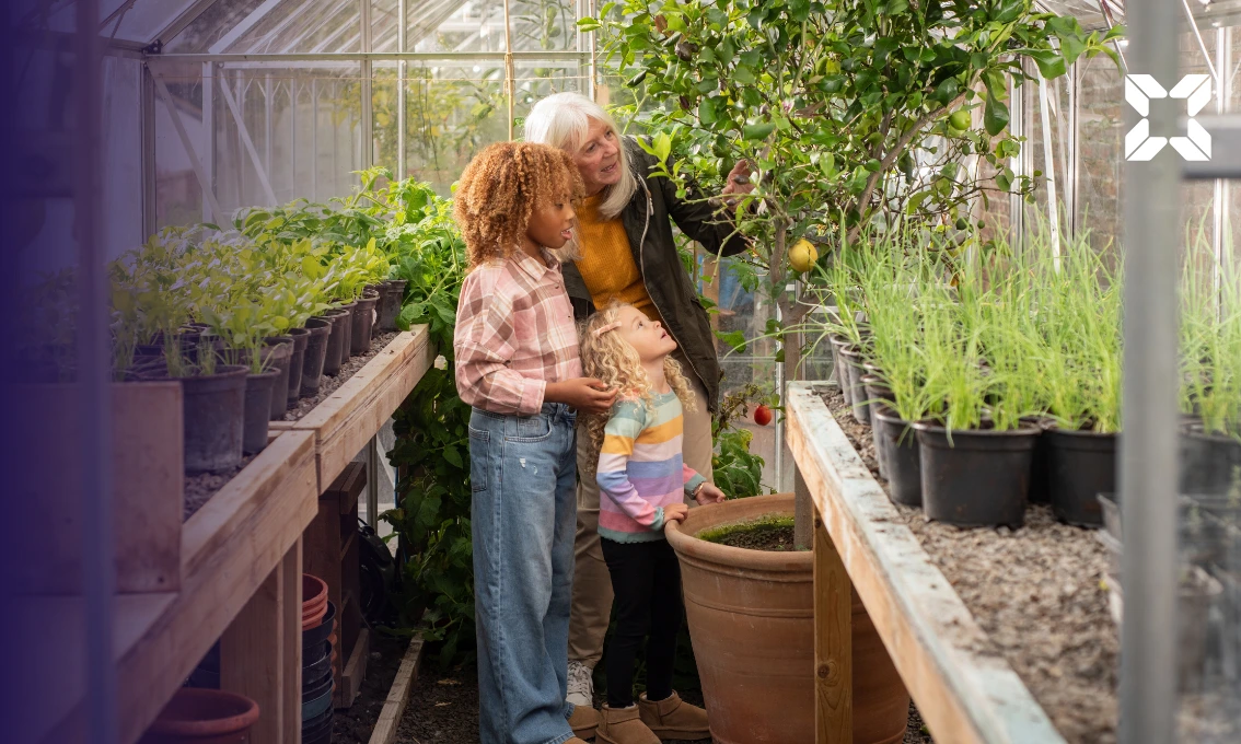A grandmother and her granddaughters are looking at a fruit tree in a greenhouse together.